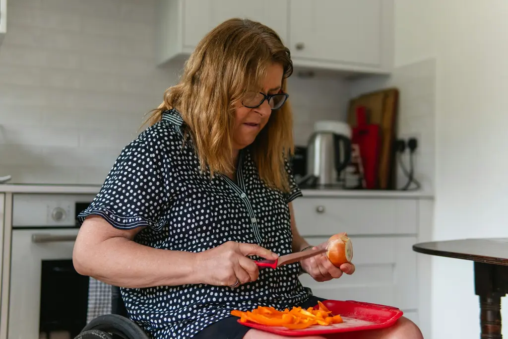 A woman who uses a wheelchair peels vegetables in her kitchen.